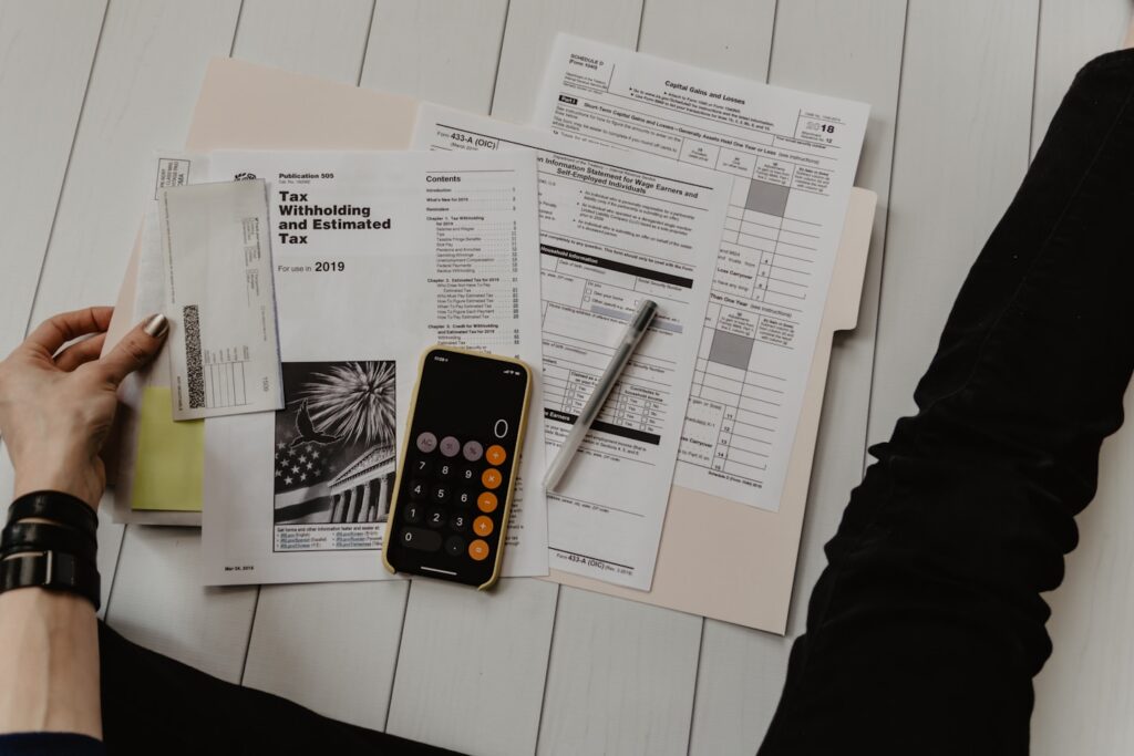 person holding paper near pen and calculator