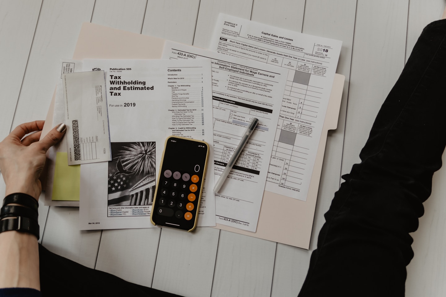 person holding paper near pen and calculator