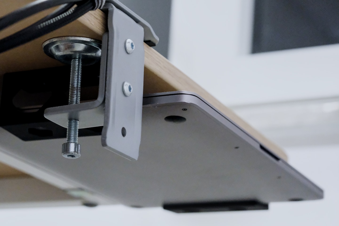 Laptop clamped under a wooden desk with cables.
