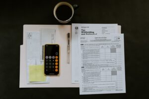 black Android smartphone near ballpoint pen, tax withholding certificate on top of white folder
