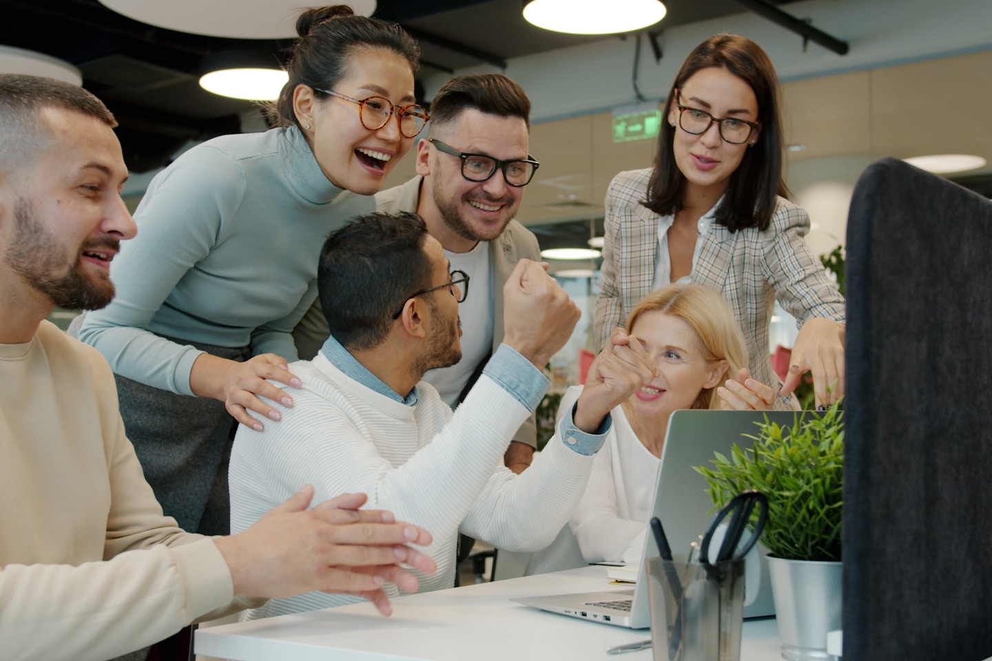 Multi-ethnic team women and men are talking clapping hands doing high-five celebrating achievement in open space office. People and work concept.